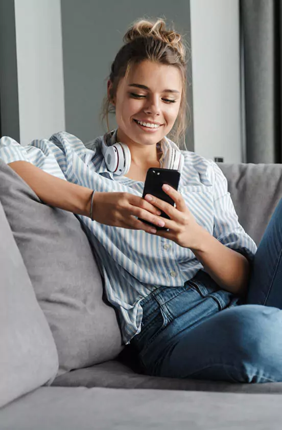 lachende Frau sitzend auf einem Sofa mit einem Handy